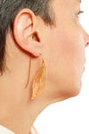 Gold leaf-shaped earring worn by a person on a white background