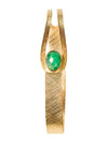 A 24 karat gold-plated bracelet with a central emerald gemstone, featuring a matte finish and textured details along the gold plating.